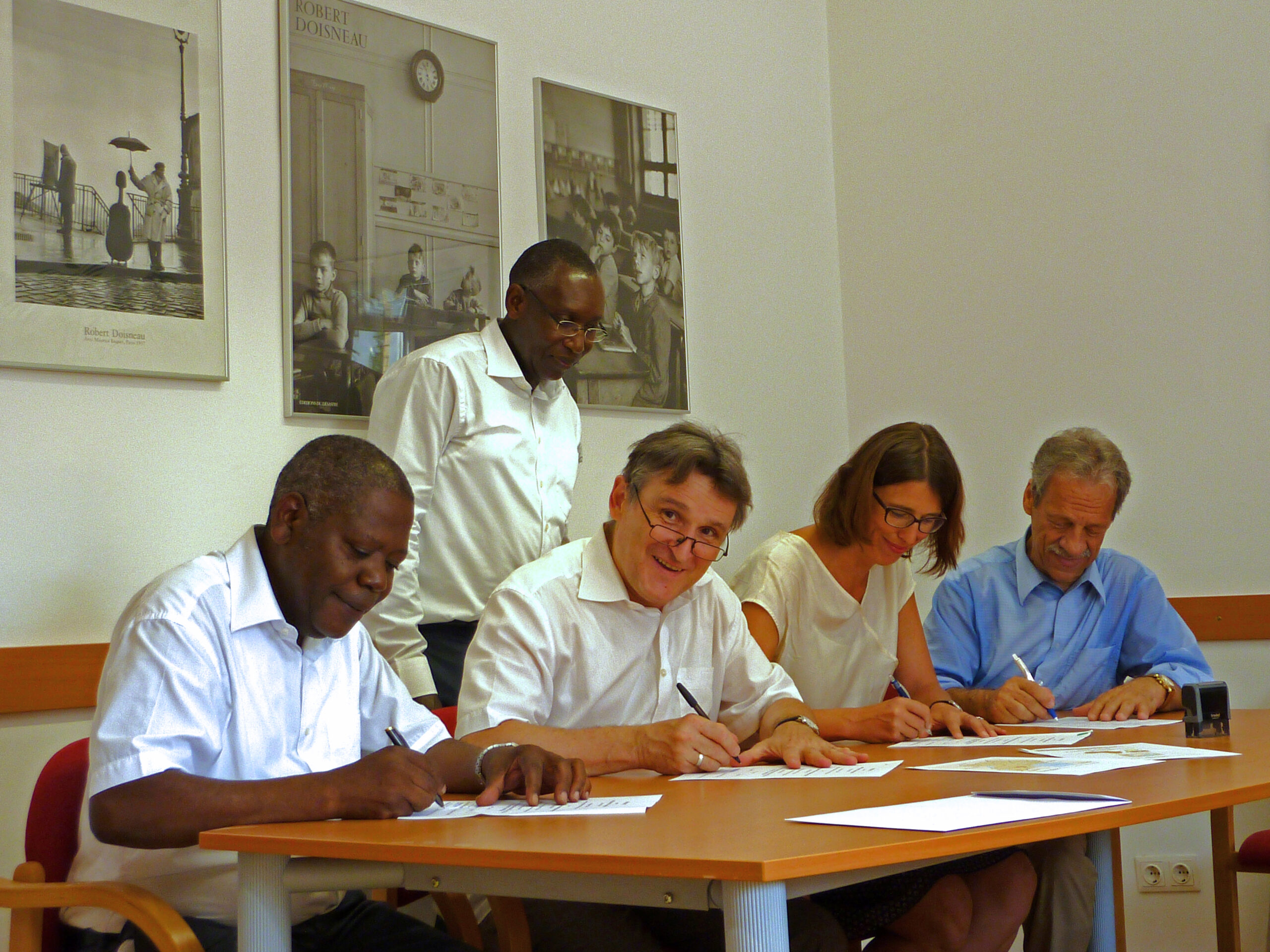 Walter Paulhart sitz mit 3 anderen Personen an einem Tisch. Alle unterzeichnen Verträge. Herr Paulhart blickt lächelnd in die Kamera.