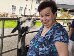 Eine Bewohnerin der betreuten Wohngemeinschaft Jedlersdorf posiert mit einem schwarz-weiß gefleckten Lama für ein Foto.