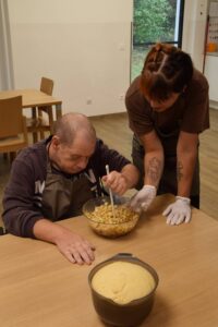 Ein Klient rührt den Teig fertig. Die Bäckerin Ramona Pillis sieht ihm dabei zu und hilft.
