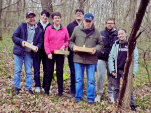 Die KlientInnen und MitarbeiterInnen der Förderwerkstätte Oberpullendorf lächeln in die Kamera. Sie stehen im Wald und einige halten Körbchen mit selbst gesammelten Bärlauch in der Hand.