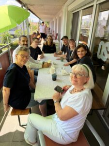 Bewohner:innen, Betreuer:innen und Besucher:innen beim gemeinsamen Kaffeetrinken auf der Terrasse.