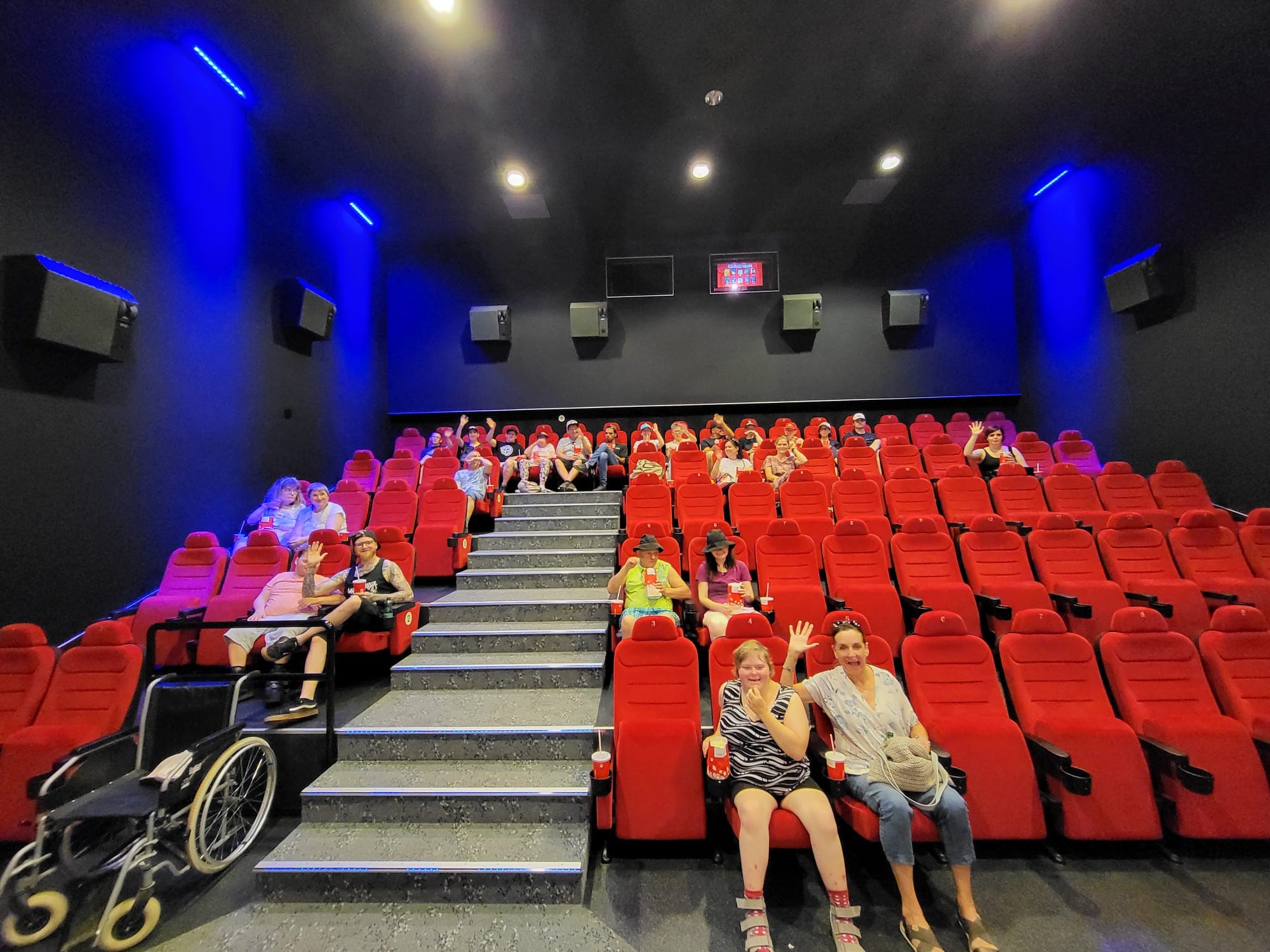 Klient:innen sitzen auf den roten Stühlen des Kinos und warten gespannt auf den Beginn des Filmes.