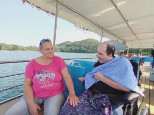 Der Bewohner Arkos sitzt lachend neben seiner Betreuerin und blickt über die Reling auf den Neusiedlersee.