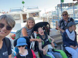 Die Bewohner:innen und die beiden Betreuerinnen des TWH St. Margarethen stehen vor dem Schiff mit dem sie gerade eine Rundfahrt gemacht haben und lächeln in die Kamera.