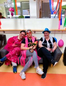 Drei Partygäste sitzen auf einer grauen Couch und lachen in die Kamera