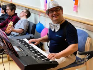 Ein junger Mann mit glitzernder Fliege und glitzerndem Hut spielt Musik auf einem Kayboard